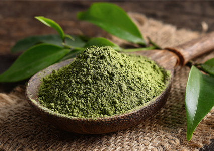 Green tea powder in a wooden bowl with leaves on a rustic background