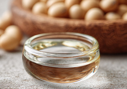 Glass container of soybean oil with soybeans in the background